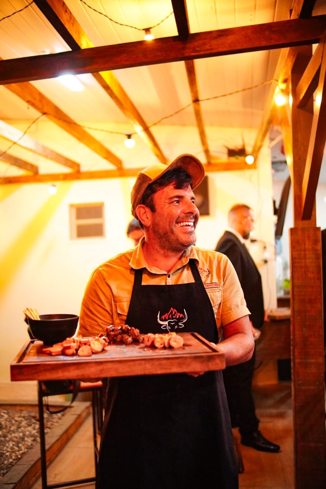 Christian Albuquerque sorrindo, servindo uma bandeja de espetinhos em um evento